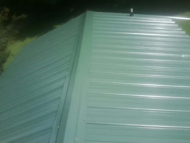 New green metal panels meeting at the ridge of a roof — Flat Roof Repair work by our crew in Holland